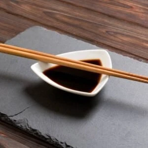 Chopsticks and soy sauce on black stone plate, wooden background